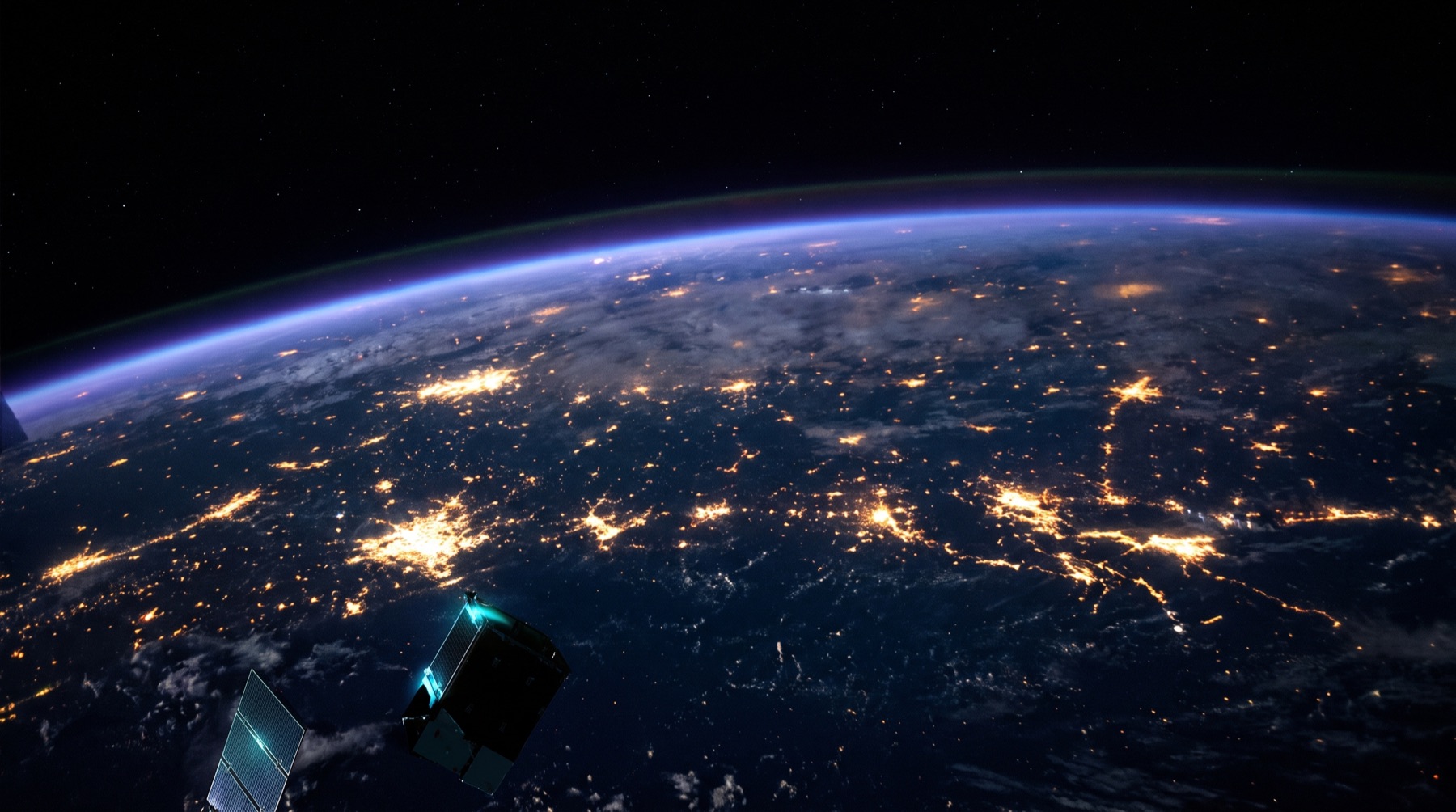 Earth's night side seen from low orbit, city lights visible through a thin atmospheric glow